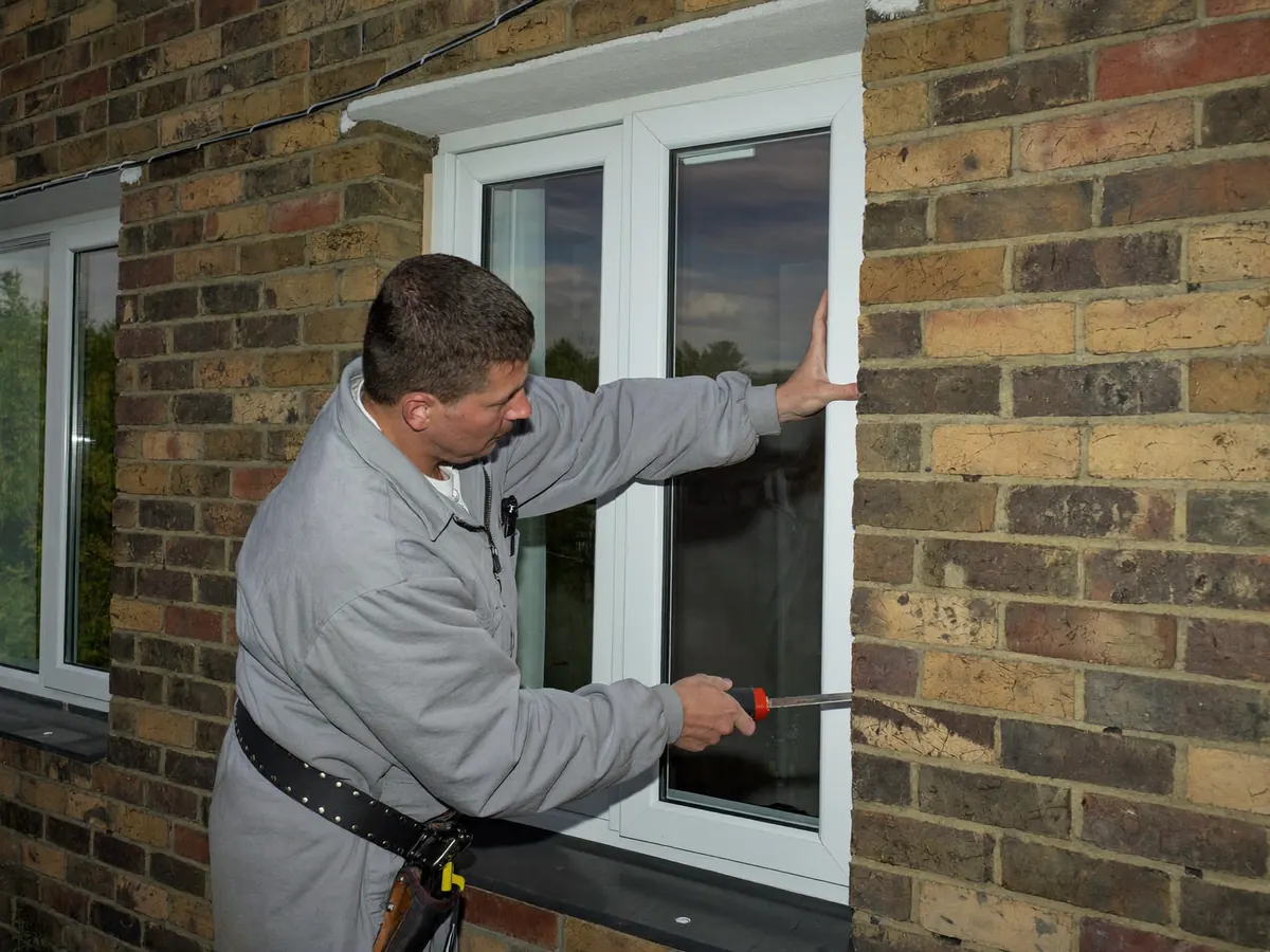 A local installer fitting a white casement window into a brick house